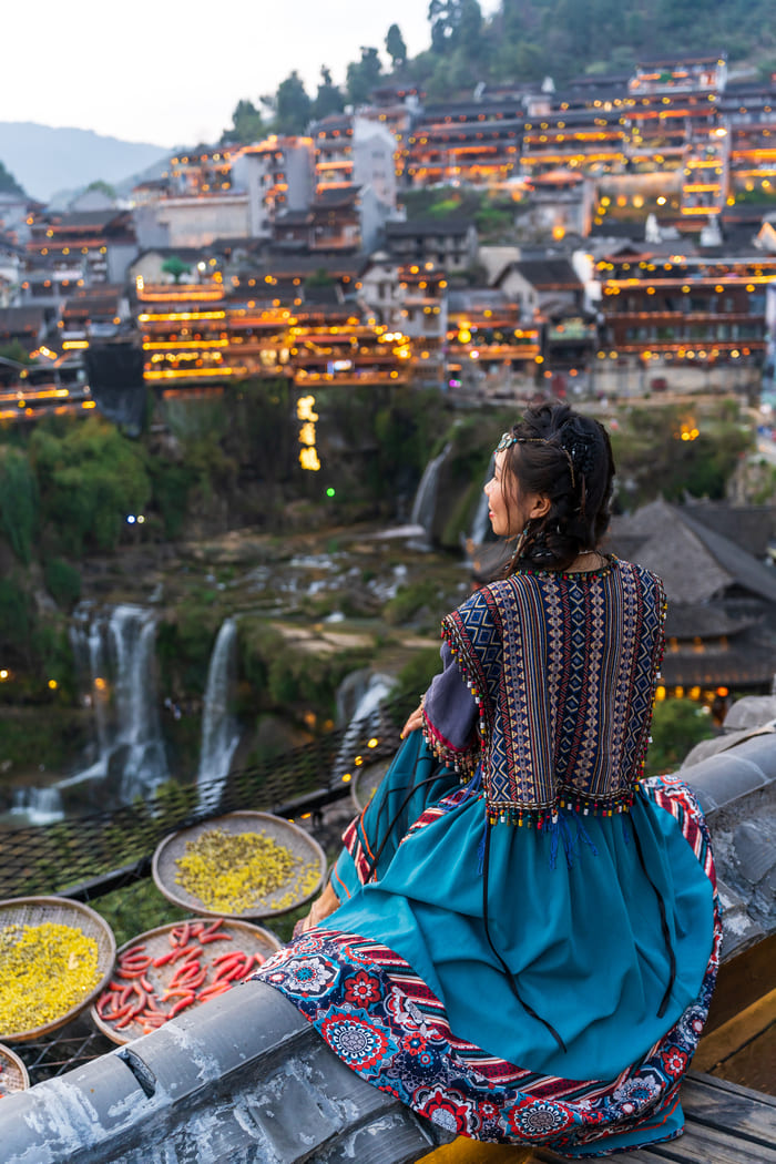 mujer sentada con vestimentas típicas chinas viendo el pueblo desde la montaña